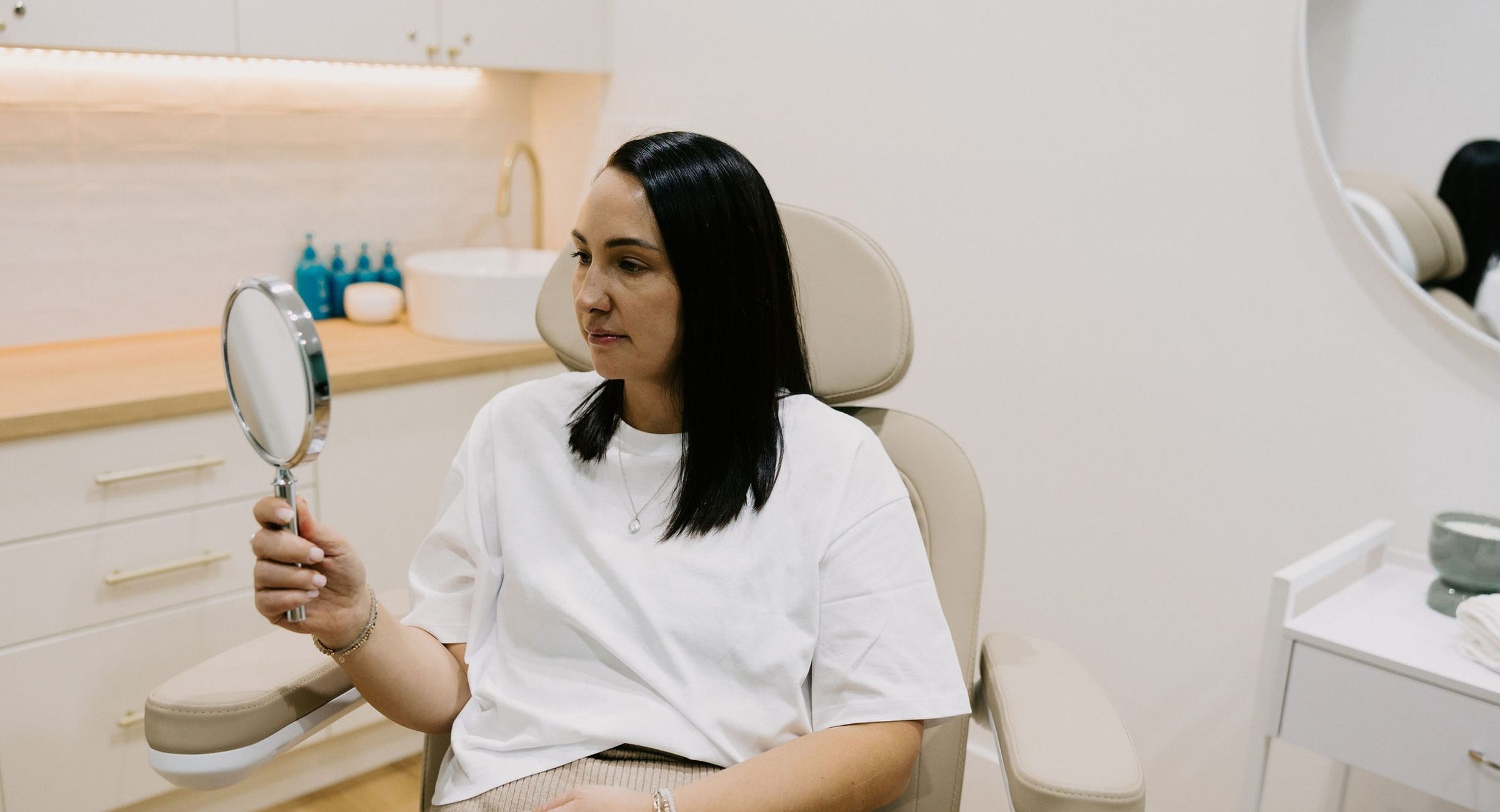 A patient seated in the treatment chair at Bloom Aesthetic Clinic, holding a mirror.